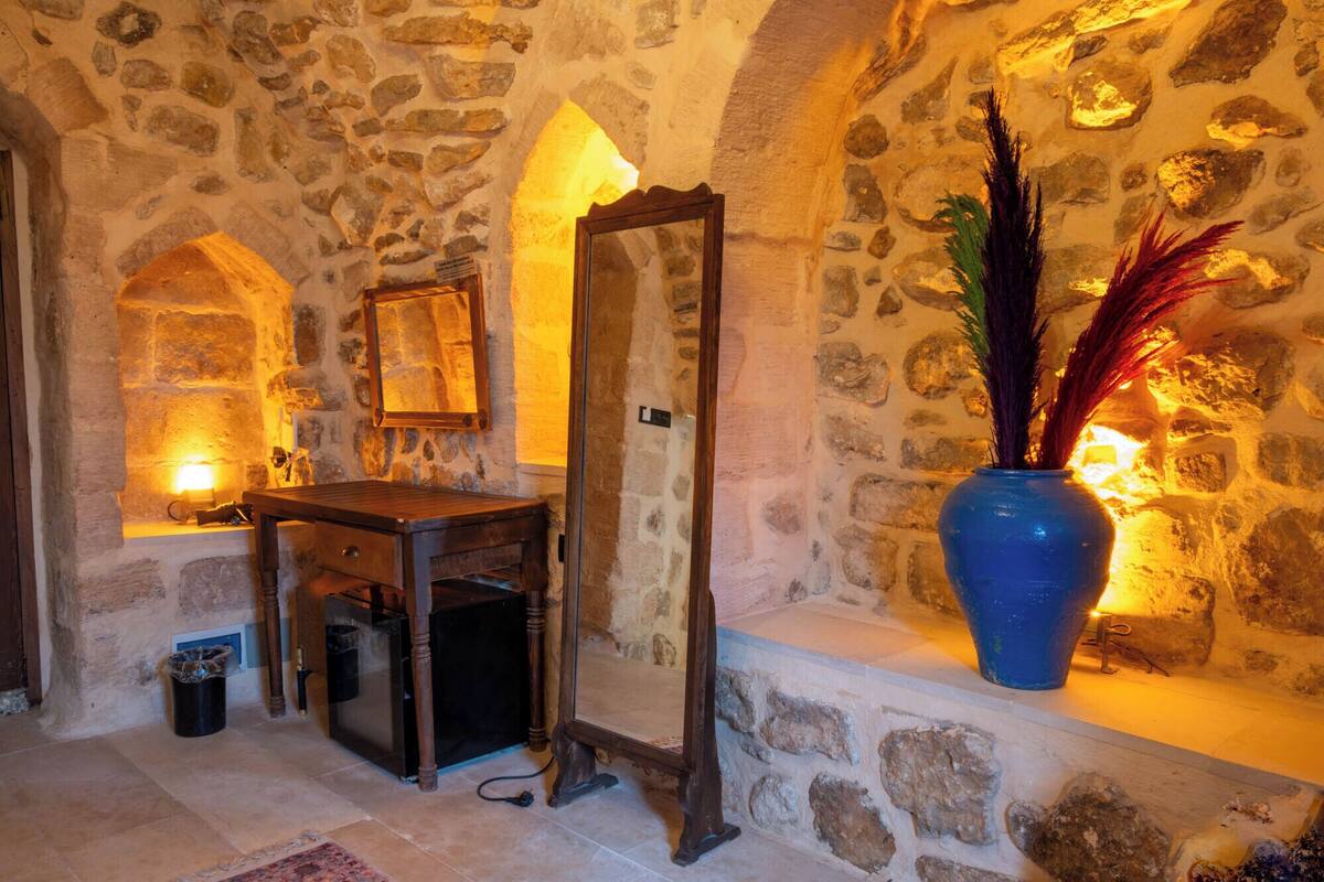 Une pièce aux murs de pierre, avec une coiffeuse en bois, un miroir et un vase décoratif contenant des plumes.