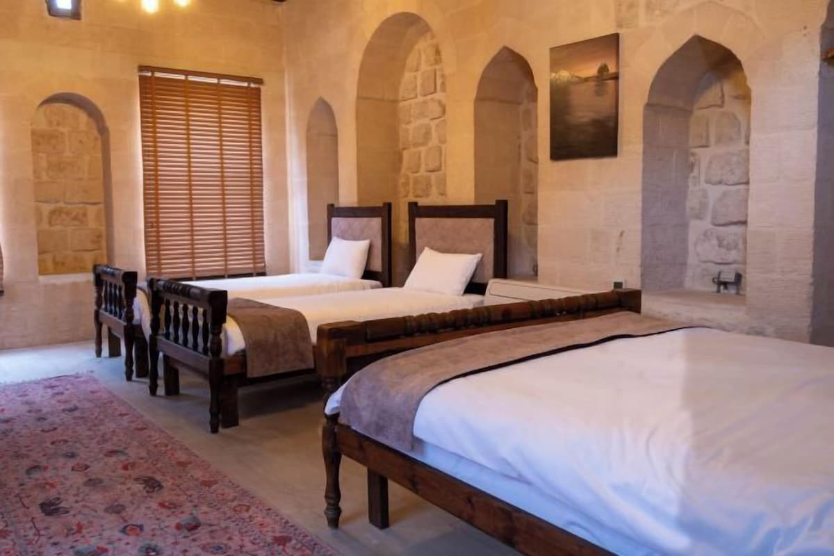 A bedroom with two beds, a wooden bench, and a patterned rug.