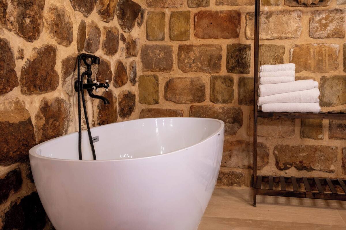 Une grande baignoire blanche, dotée d’un robinet noir, placée devant un mur en pierre.