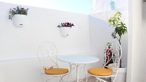 Una pequeña zona de estar al aire libre con dos sillas y una mesa, paredes blancas y plantas en macetas.