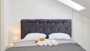 Un lit bien fait, avec une tête de lit capitonnée, deux oreillers, une table de chevet avec une lampe et un verre de jus d’orange.