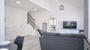 Un salon moderne avec un canapé gris, un téléviseur à écran plat et un escalier menant à un autre niveau.