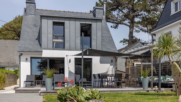 A modern two-story house with a patio area featuring outdoor furniture and a covered seating area.