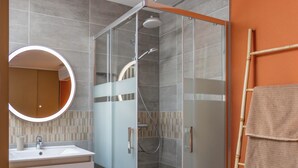A modern bathroom with a glass-enclosed shower, a vanity with a mirror, and a towel rack.