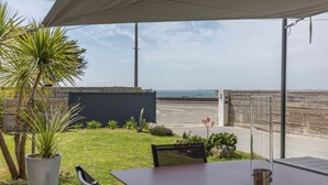 An outdoor patio with a table and chairs, a potted plant, and a view of the sea.