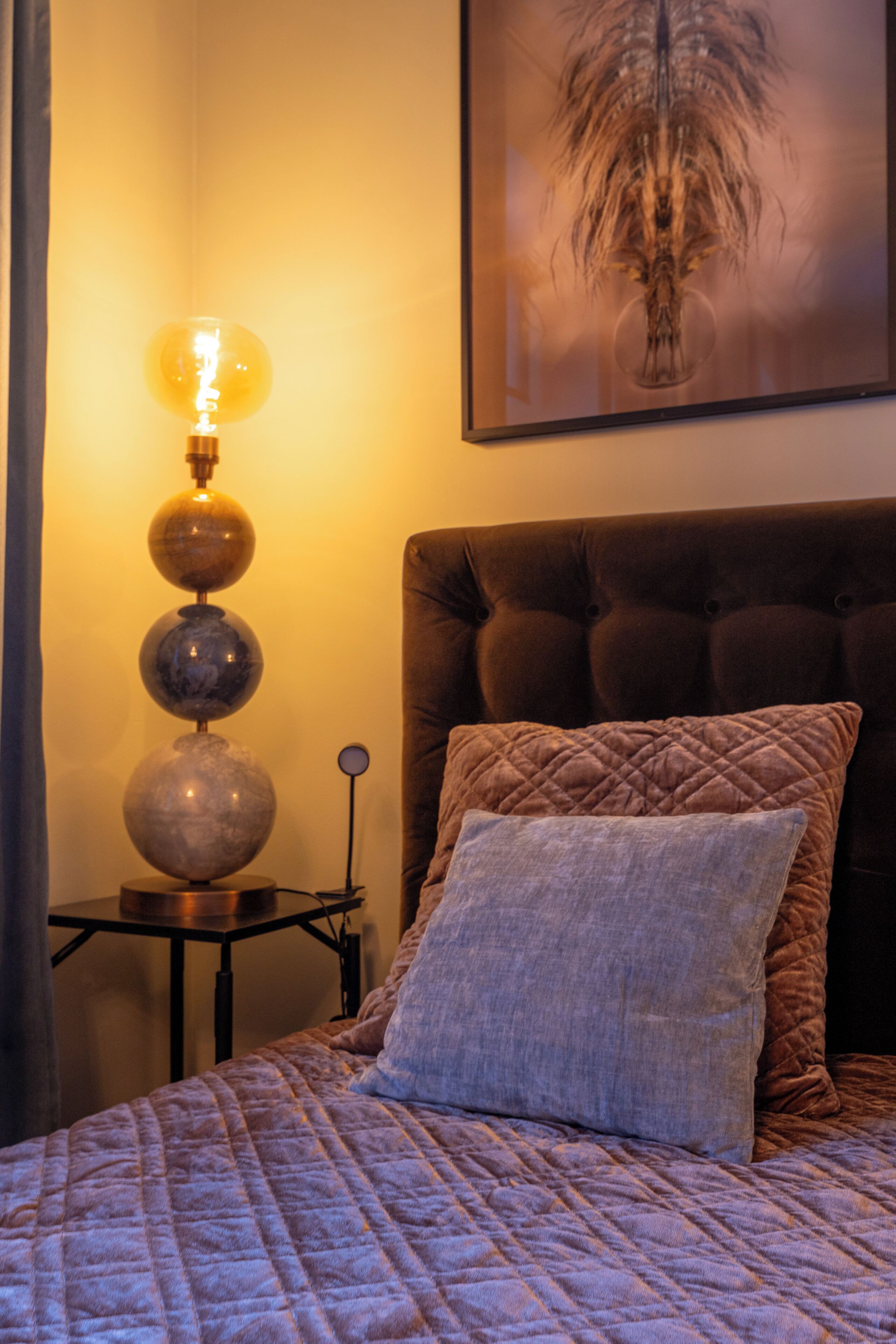 A bedroom with a bed, a wall-mounted lamp, and a framed artwork.