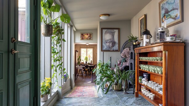 A hallway with a green door, potted plants, a wooden bookshelf, and a dining area in the background. - The White brig (Hudiksvall)
