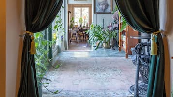 A hallway with dark curtains, a patterned rug, and a dining area with chairs and plants.