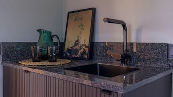 A kitchen with a granite countertop, a stainless steel sink, a green vase, and a framed artwork.