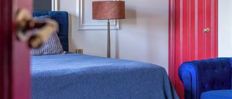 A bedroom with a bed, a blue chair, a red door, and a patterned rug.