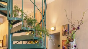 A spiral staircase with greenery, a rustic table with potted plants, and a wall-mounted vase with flowers. - The White brig (Hudiksvall)
