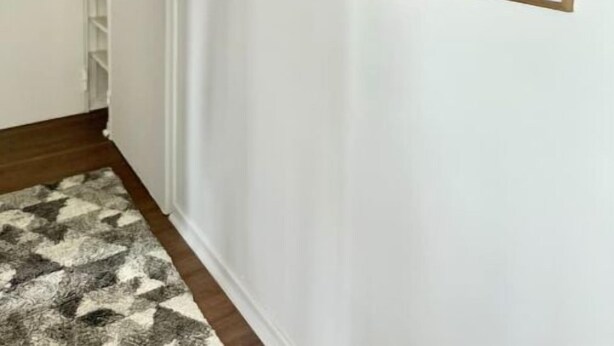 Un pasillo con un rug decorativo, paredes blancas y documentos enmarcados en la pared.