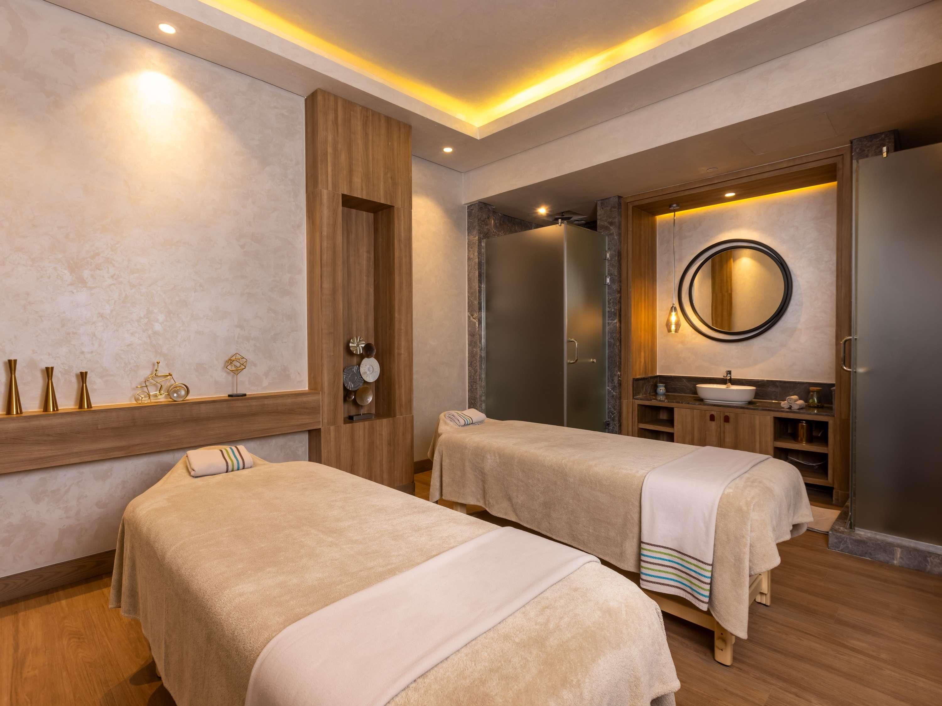 Ein Wellnessraum mit zwei Massageliegen, einem Holzschrank, einem Spiegel und einem Waschbecken.