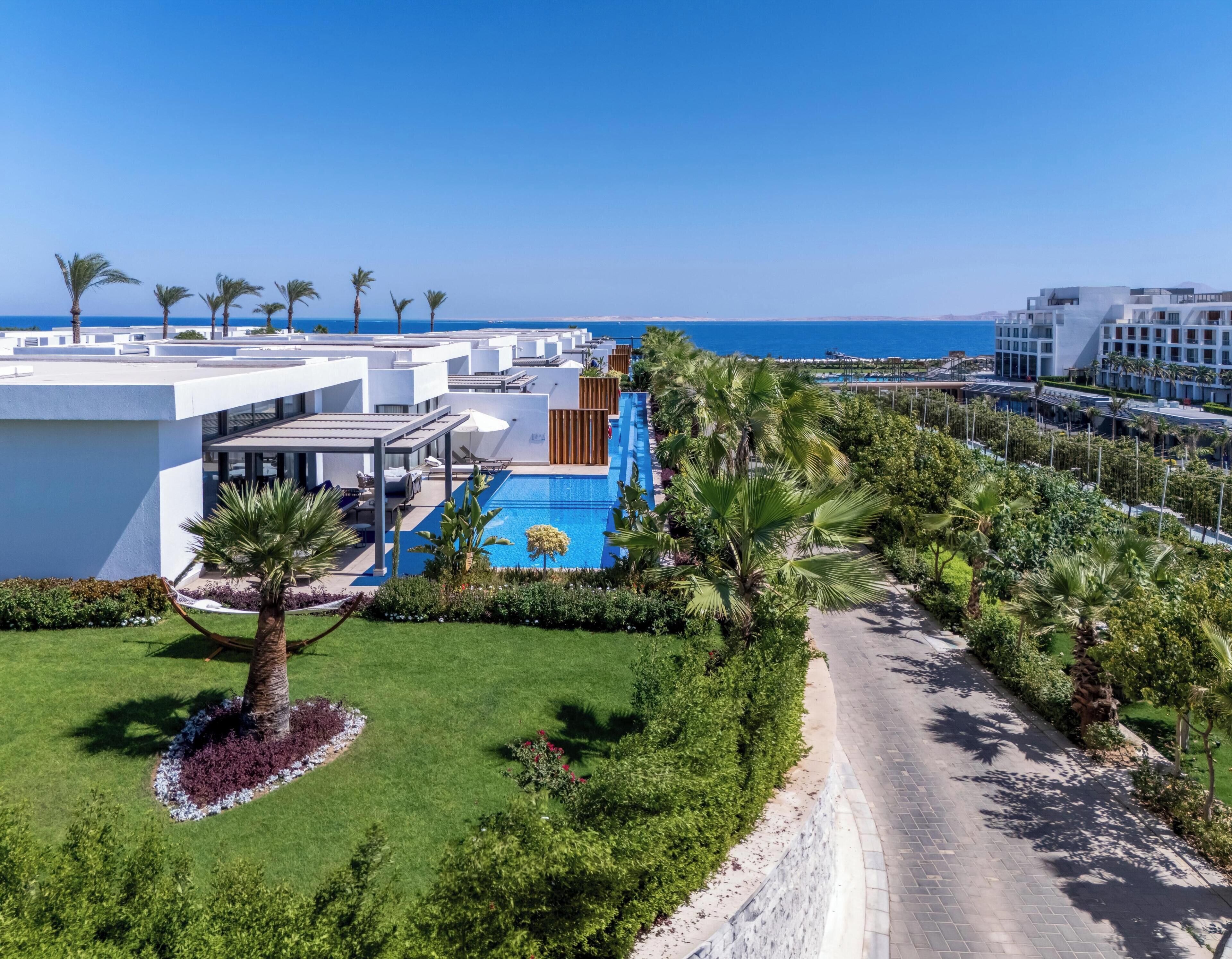 A resort with a swimming pool, palm trees, and a view of the sea.
