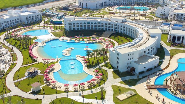 A resort with multiple swimming pools, a central fountain, and a large building with a curved facade.