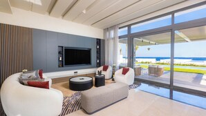A modern living room with a large TV, comfortable seating, and a view of the ocean.