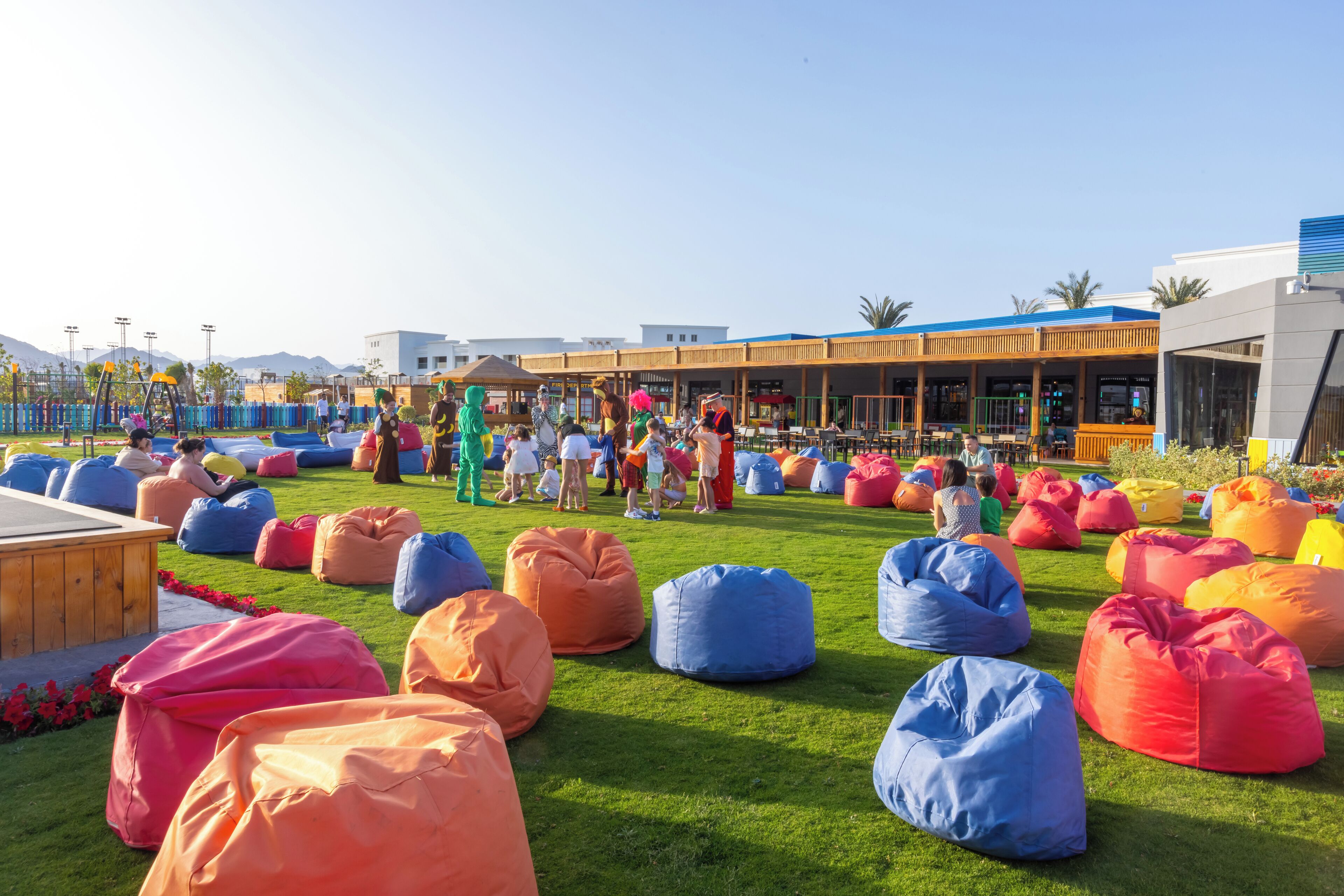 A grassy outdoor area with colorful bean bags and a building with a blue roof in the background.