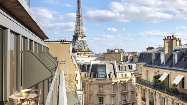 A view of the Eiffel Tower from a high-rise building with balconies, a table with chairs, and a window overlooking the tower. - Hotel Maison Hamelin Paris - Handwritten Collection (Paris)