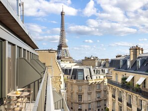 A view of the Eiffel Tower from a high-rise building with balconies, a table with chairs, and a window overlooking the tower.