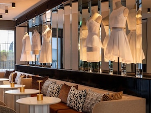 Un hall d’hôtel moderne doté d’un espace salon, d’un mur recouvert de miroirs où sont exposés des vêtements, et offrant une vue sur l’extérieur.