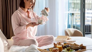 A person in a hotel room holding a cup, with a breakfast tray on the bed. - Hotel Maison Hamelin Paris - Handwritten Collection (Paris)
