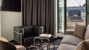A modern hotel room with a black leather armchair, a glass coffee table, and a sofa. A large window offers a view of the cityscape. - Hotel Maison Hamelin Paris - Handwritten Collection (Paris)