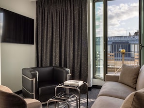 Ett modernt hotellrum med en svart läderfåtölj, ett soffbord i glas och en soffa. Ett stort fönster erbjuder utsikt över stadsbilden.