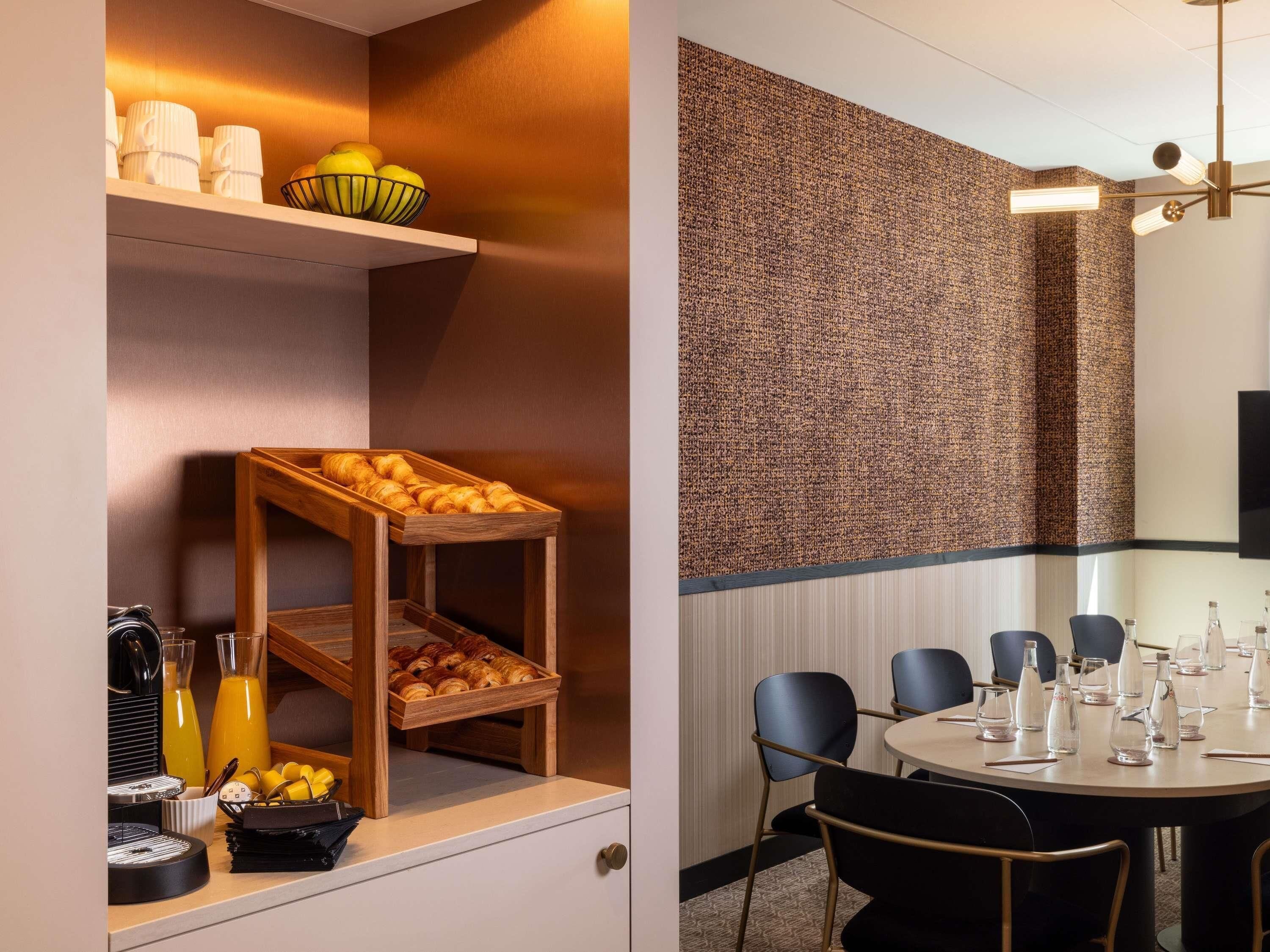 A breakfast bar with croissants, a fruit bowl, and juice dispensers.
