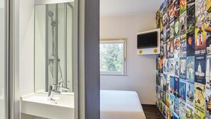 A bathroom with a shower, a sink, a bed, and a wall with travel posters. - hotelF1 Genève Saint-Julien-En-Genevois (Rénové) (Viry)