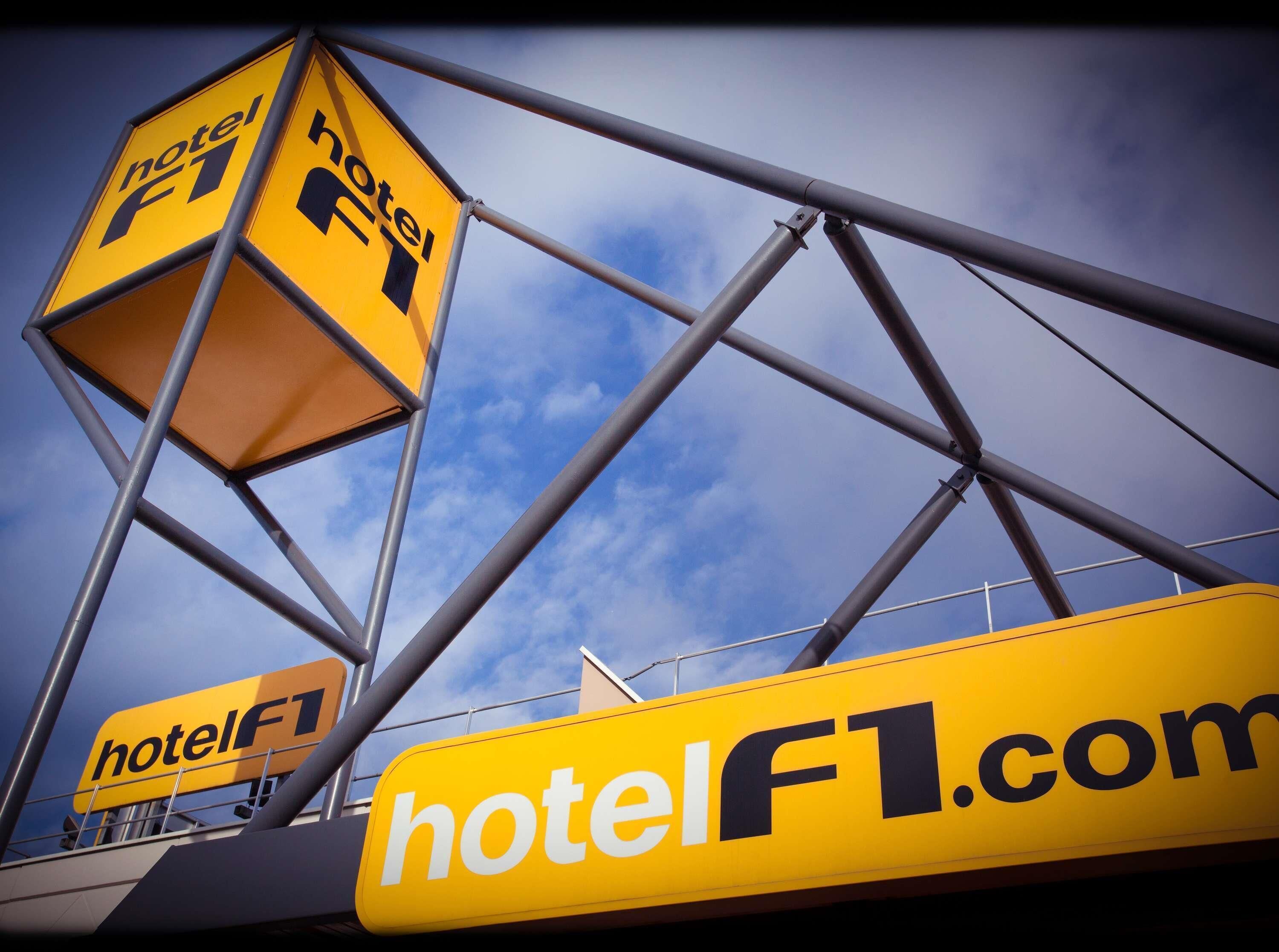 A yellow sign with the text "hotelF1.com" and a logo with a stylized 'F1' and a hotel icon.