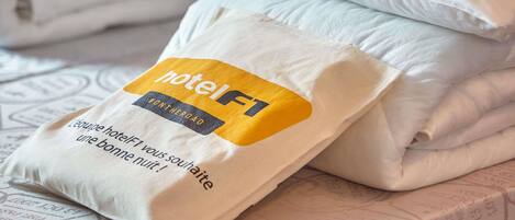 A neatly folded white pillow with a HotelF1 tag on it, placed on a bed with a patterned bedspread.