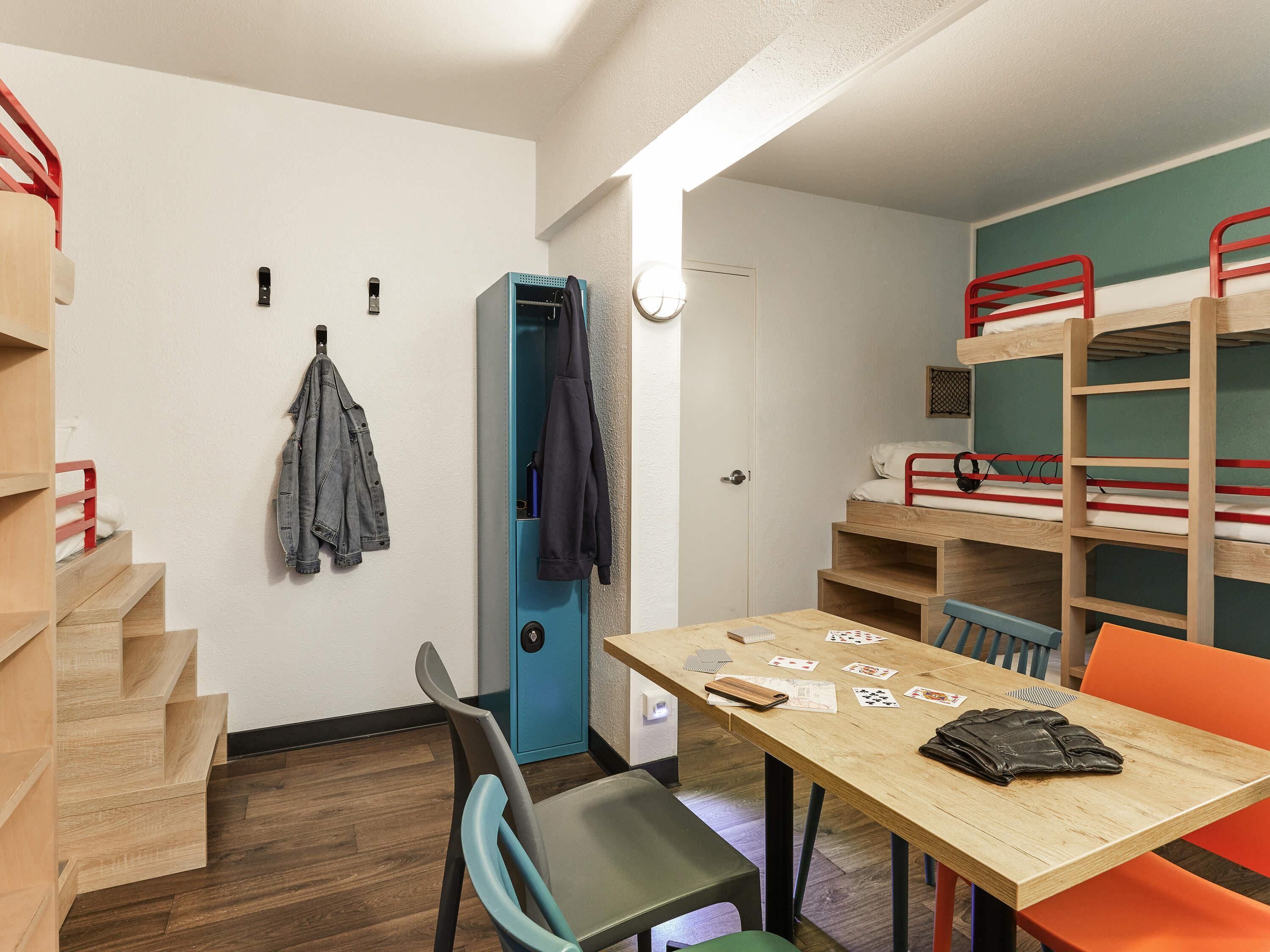 A dormitory room with bunk beds, a desk with cards, a chair, and a coat rack.