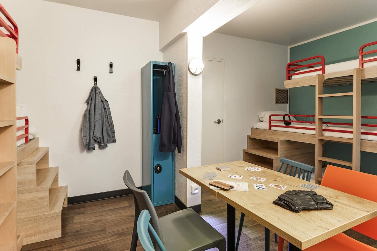 A dormitory room with bunk beds, a desk with cards, a chair, and a coat rack.