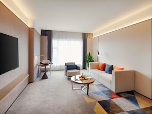 Ein modernes Hotelzimmer mit Sofa, Sessel, Couchtisch und Flachbildfernseher.