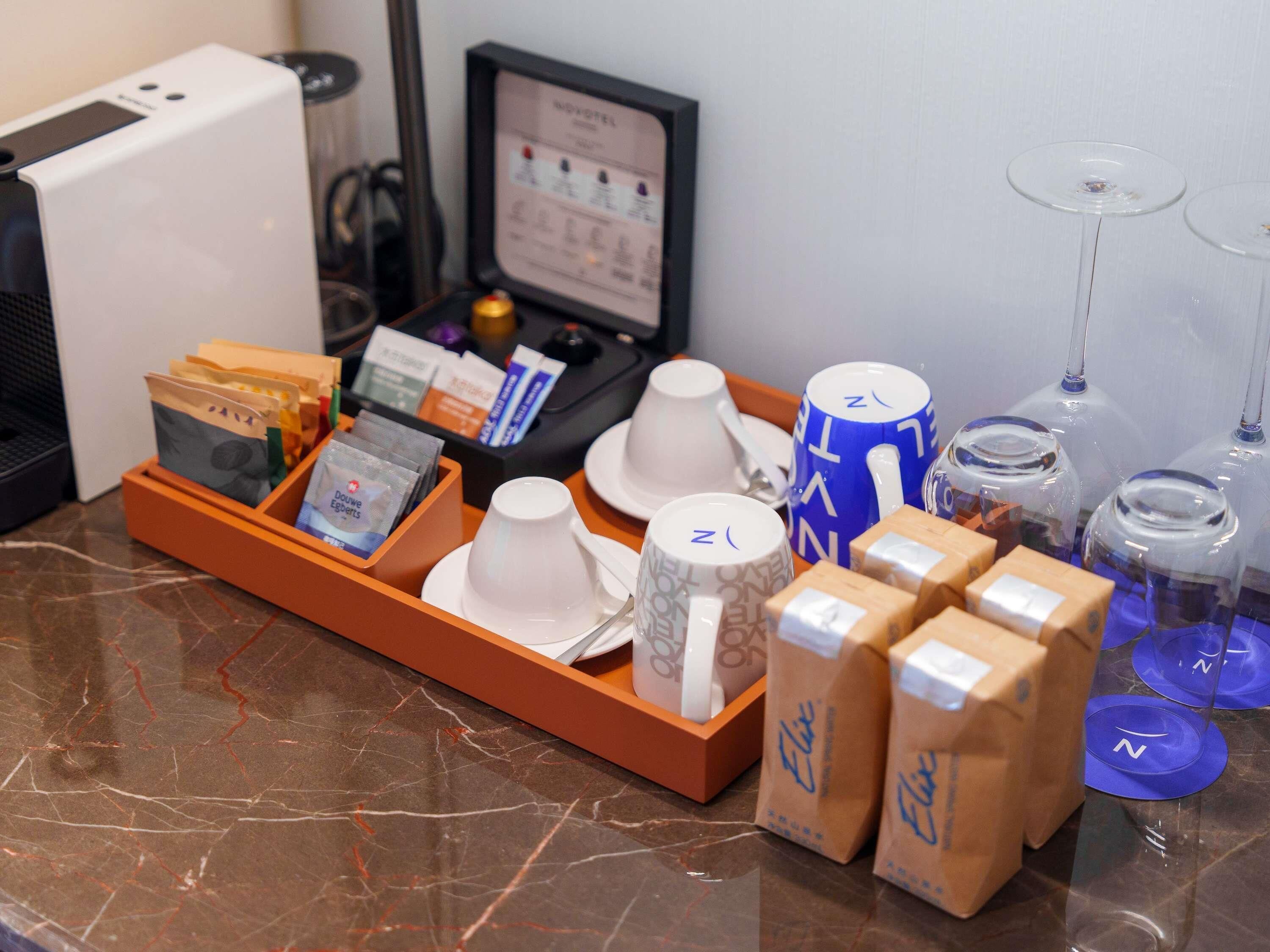A hotel room with a marble countertop, a tray with tea bags, cups, and a minibar.