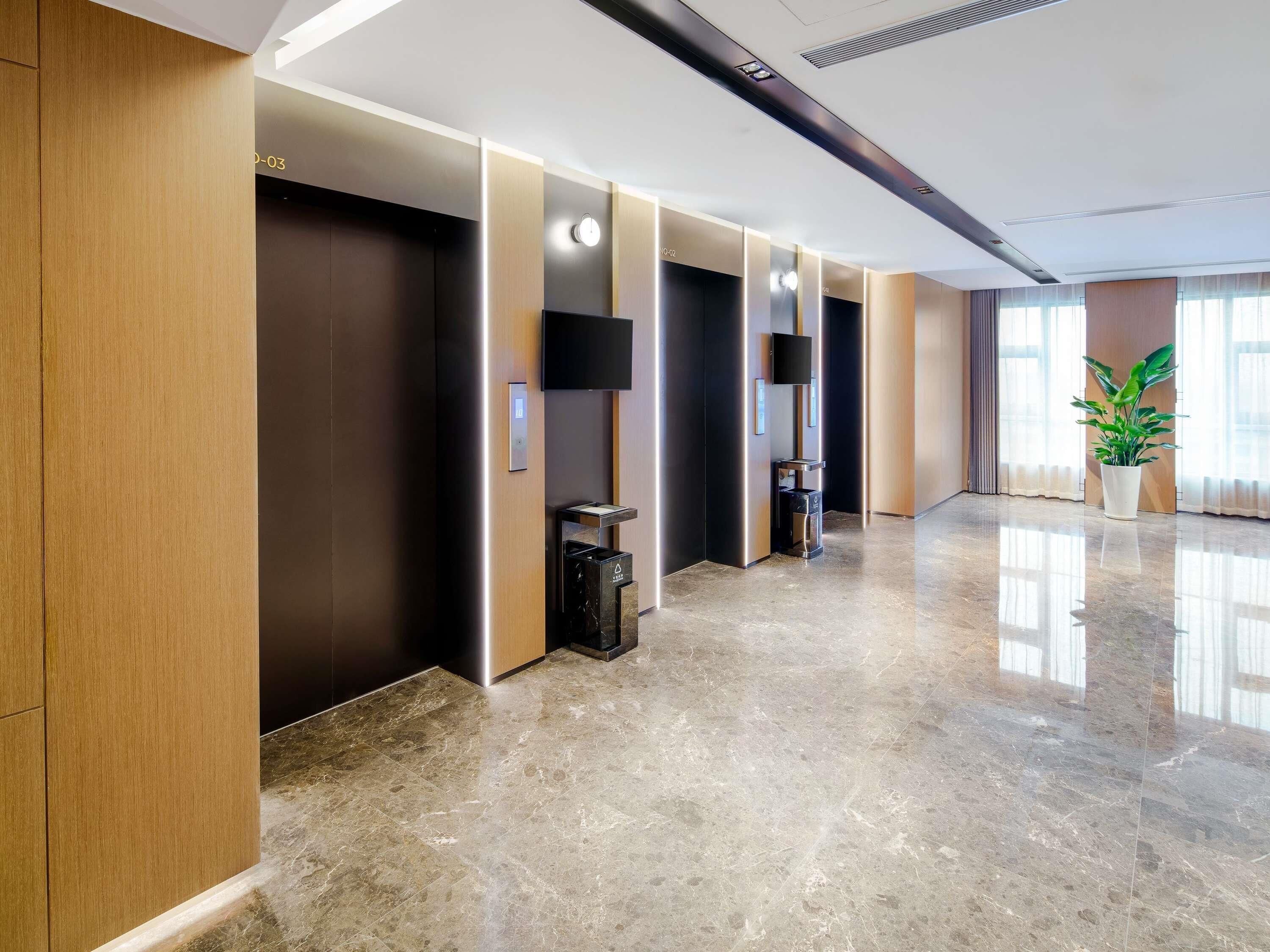 Un hall d’hôtel moderne avec un sol en marbre poli, des lambris en bois et une plante en pot.