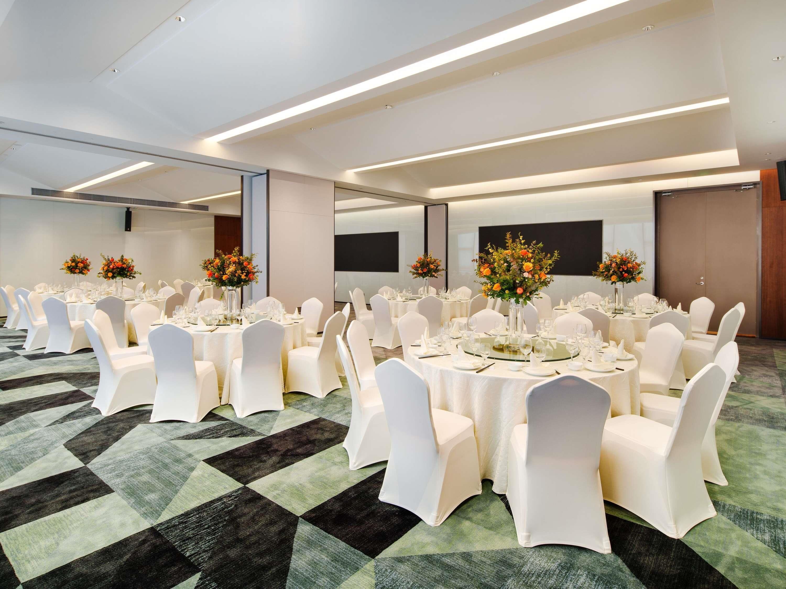 A conference room with round tables, white chairs, and floral centerpieces.