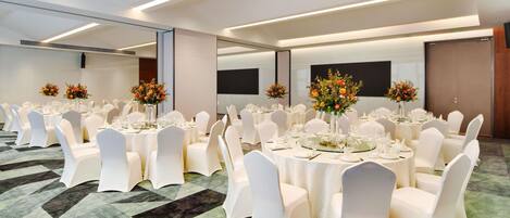 A conference room with round tables, white chairs, and floral centerpieces.