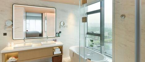 Un baño moderno con un espejo grande, lavamanos dobles, una bañera y vistas a través de una puerta de vidrio.