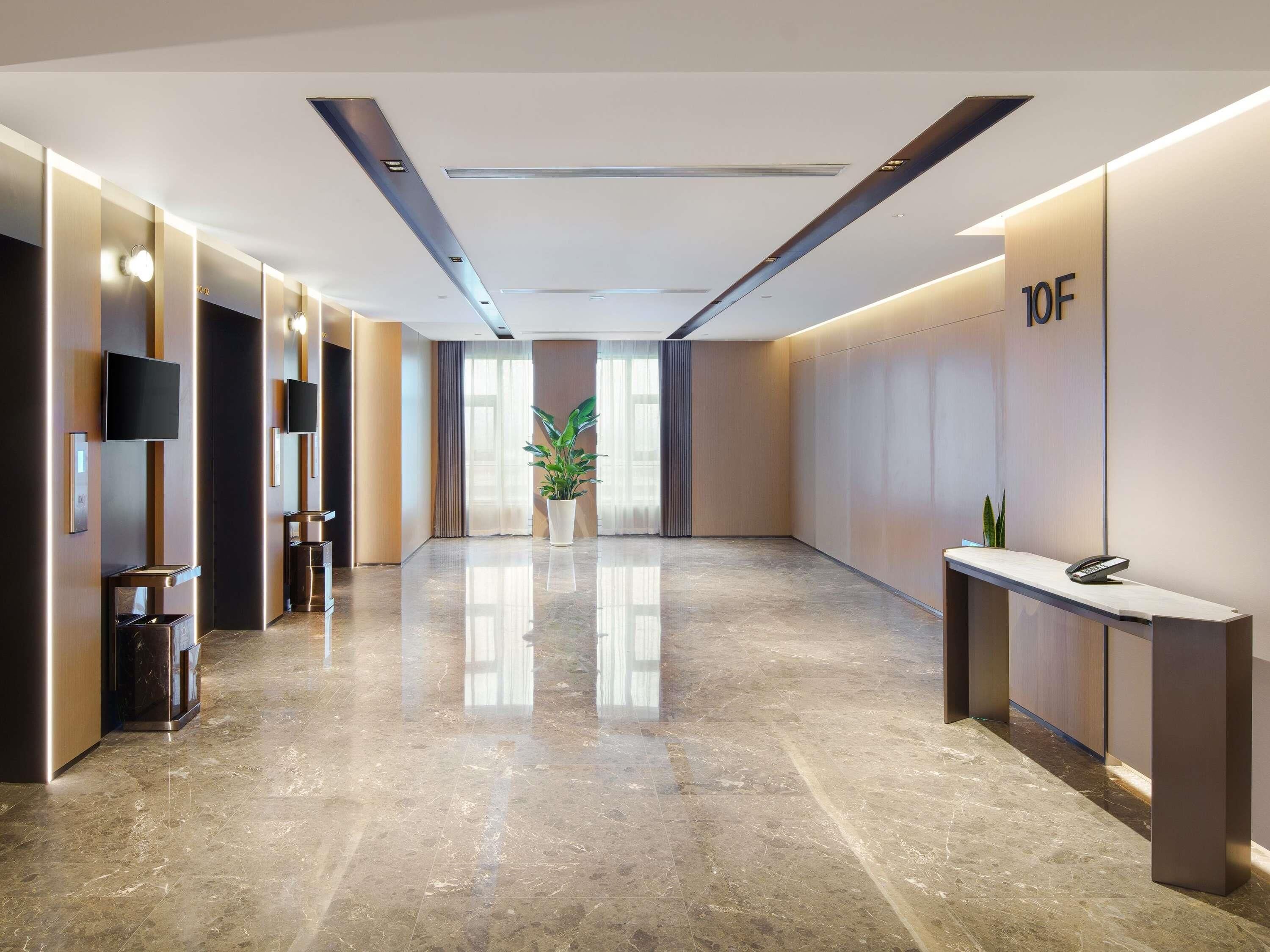A modern hotel lobby with a polished marble floor, a reception desk, and a large potted plant.