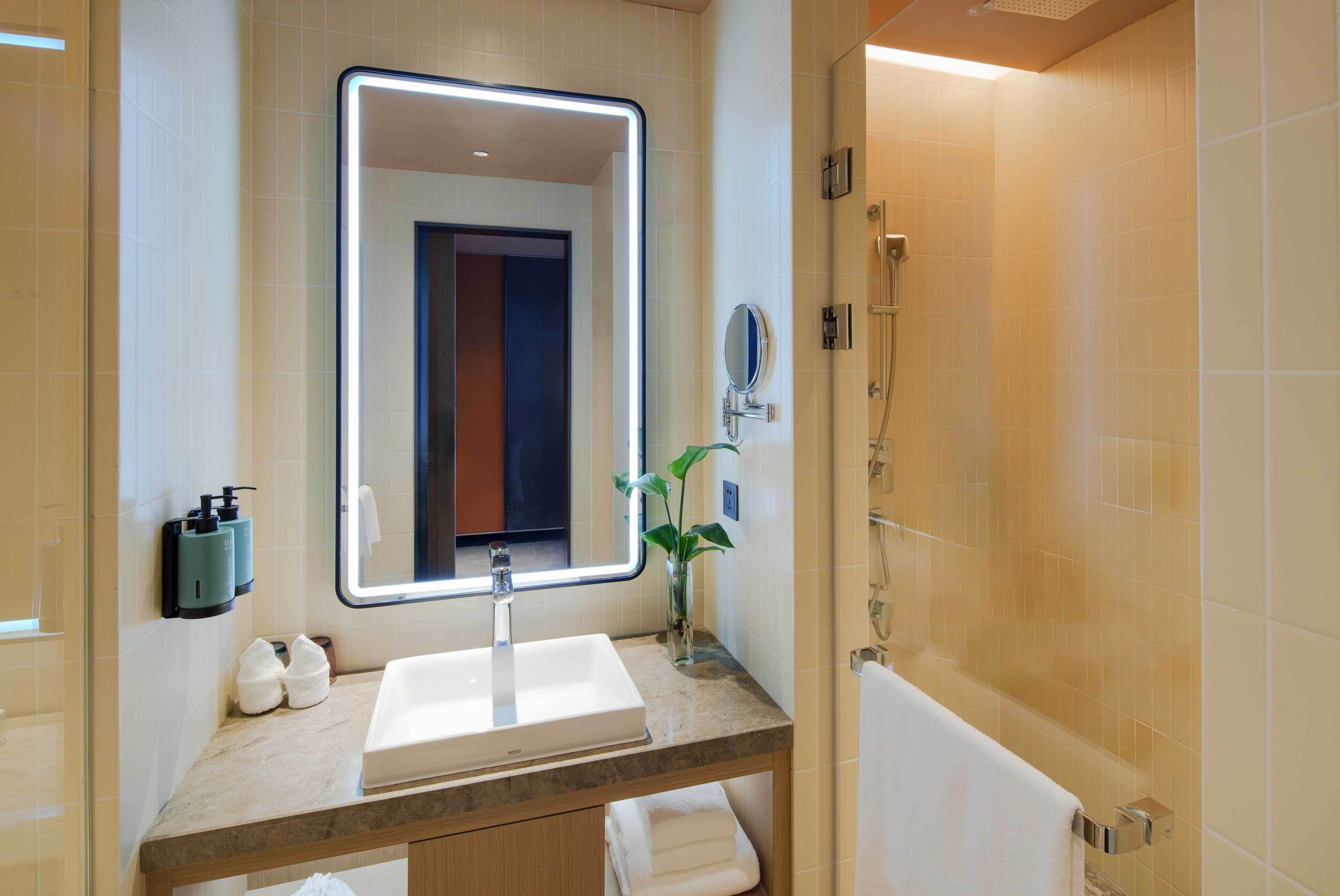 A bathroom with a large mirror, a sink, a shower, and a towel rack.