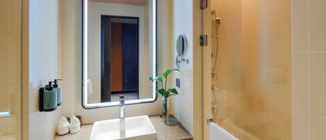 A bathroom with a large mirror, a sink, a shower, and a towel rack.