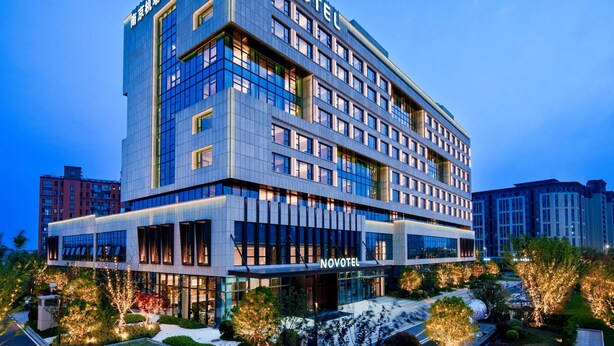 A modern hotel building with multiple floors, large windows, and a prominent 'NOVOTEL' sign.