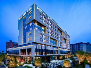 Un hôtel moderne, avec plusieurs étages, de grandes fenêtres et une enseigne « NOVOTEL » bien visible.