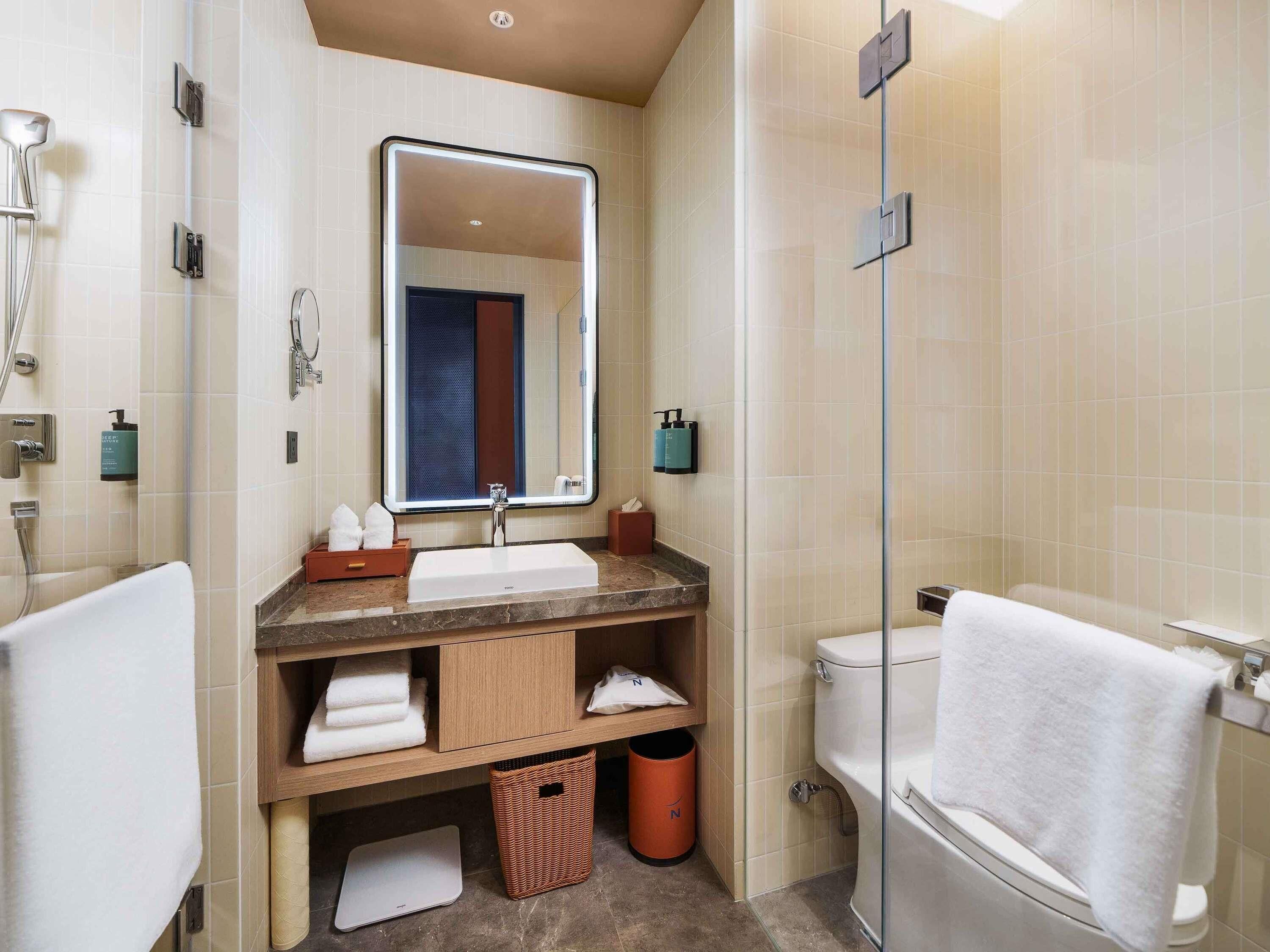 A modern bathroom with a large mirror, a sink, a toilet, and a shower.