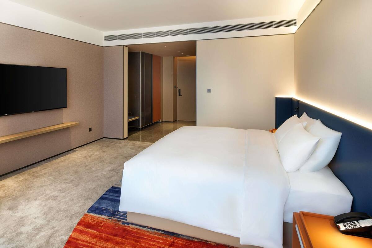 A hotel room with a large bed, a bedside table with a phone, a flat-screen TV mounted on the wall, and a walk-in closet.