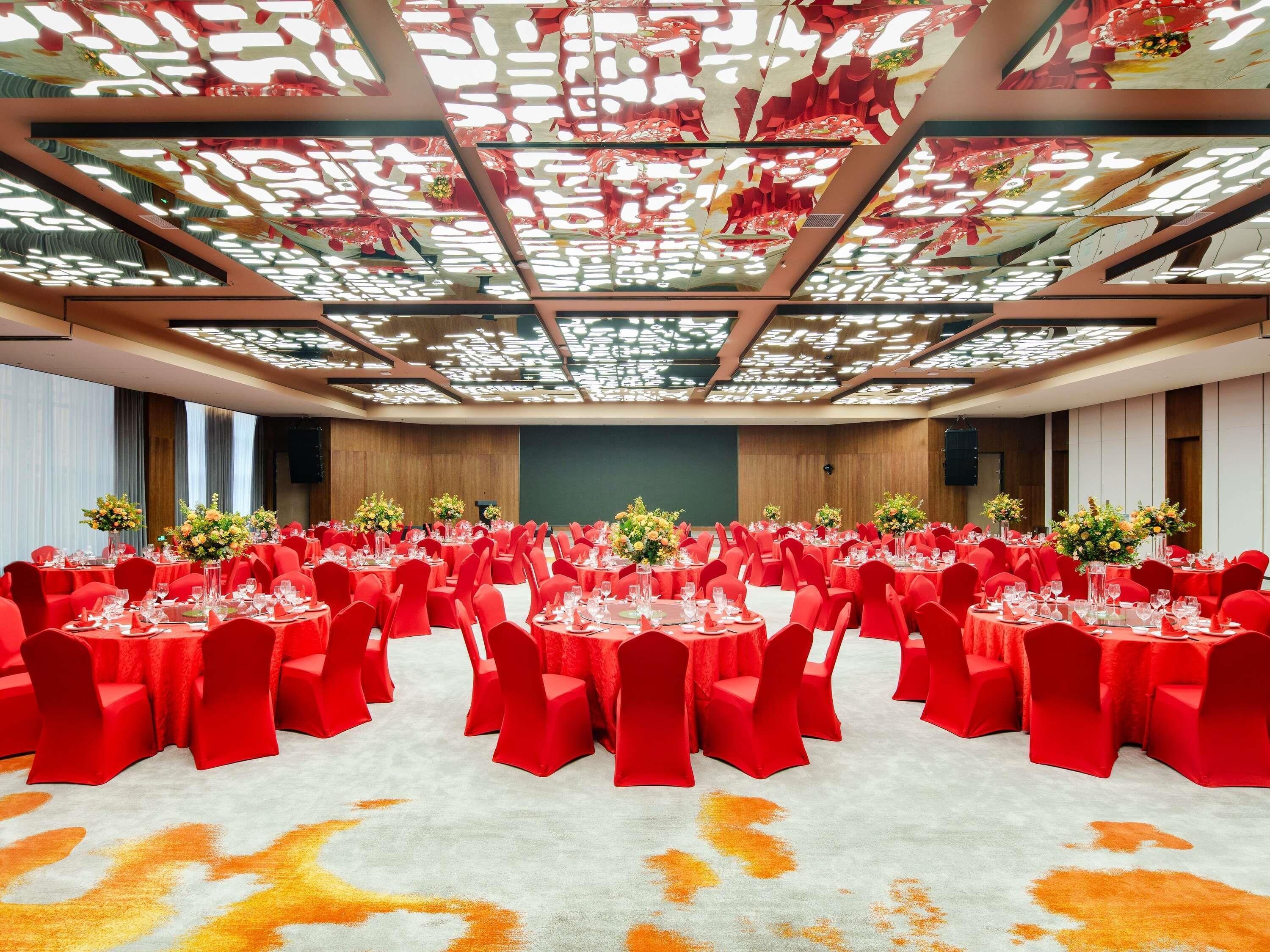 A banquet hall with round tables, red chairs, and floral centerpieces.