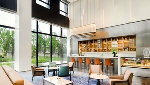 A modern hotel lobby with a bar area, seating arrangements, and large windows offering a view of greenery.
