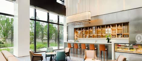 Un hall d’hôtel moderne doté d’un bar, de différents espaces de détente et de grandes fenêtres donnant sur un paysage verdoyant.