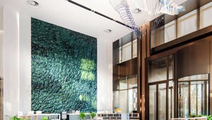 A modern lobby with a large green wall, a central orange sofa, and a patterned carpet.